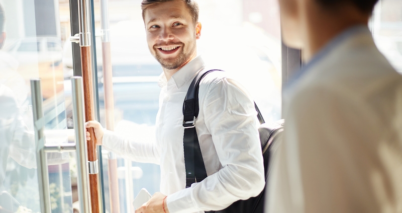 Young man with trendy backpack walking out of cafe door and smiling over back saying goodbye