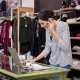 Young businesswoman talking over phone while checking laptop in her clothing store. Young entrepreneur in casual using laptop and talking on mobile. Store manager woman checking important documents on laptop. Small business concept.