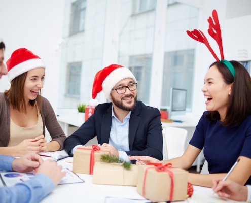 Cheerful employees in Santa caps laughing at Christmas meeting