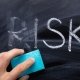 Close-up Of Person's Hand Erasing Risk Text With Blue Sponge
